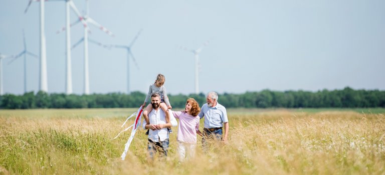 Drei Generationen einer Familie spazieren vor Windkraftanlagen durch ein Kornfeld